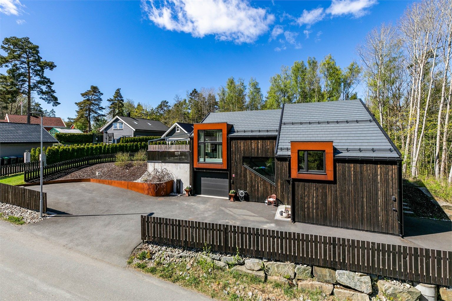 Stakittgjerde rundt gårdsplassen og del av hagen er beiset i samme nyanse som boligens kledning.