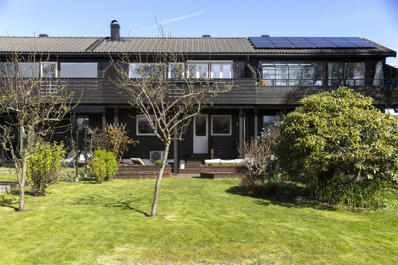 Fasaden mot hagen viser de to uteplassene: den romslige balkongen i toppetasjen og markterrassen på bakkeplan.