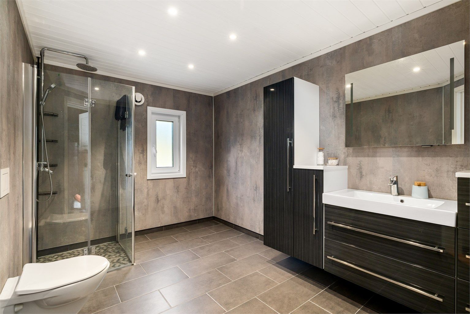 STILRENT: Grå matchende fliser på gulv og våtromsplater på vegger - baderomsinnredningen er fra Lind Bad.