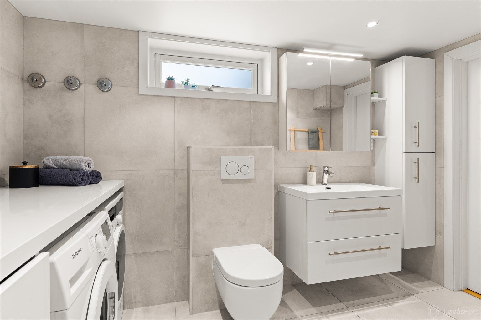 Innredningen inkluderer vegghengt servantmøbel, speilskap med belysning og ekstra høyskap for oppbevaring.