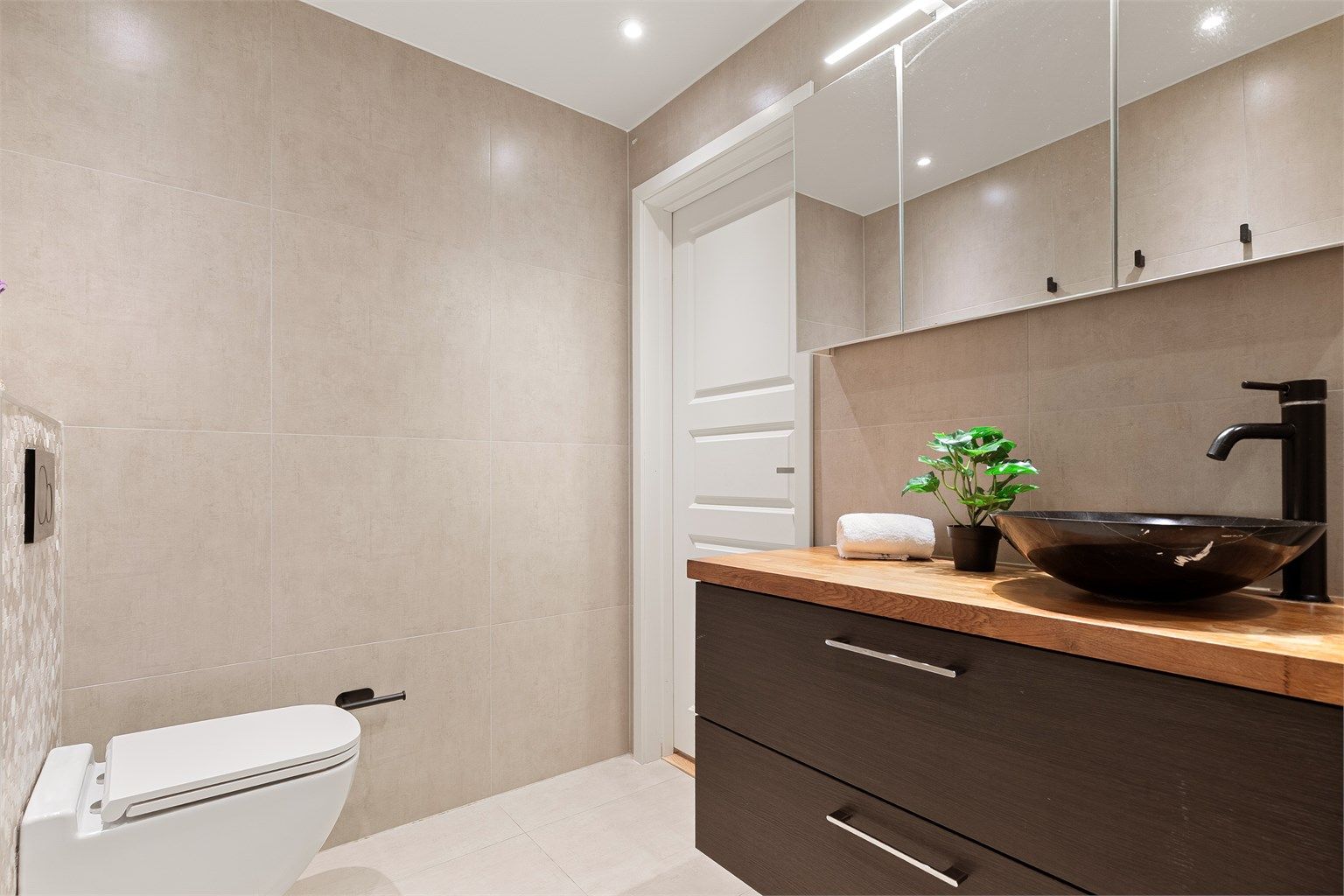 Bad med moderne innredning, vegghengt toalett og downlights i taket.