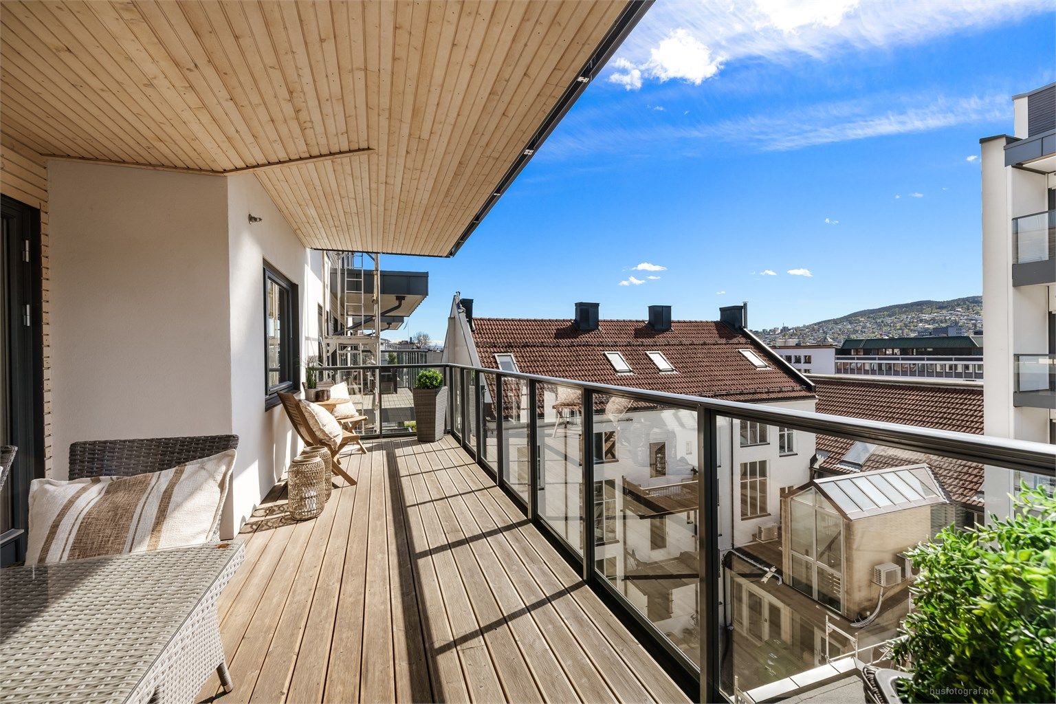 Balkongen er i betongkonstruksjon med rekkverk av metall og glass, og terrassebord på gulvet.
