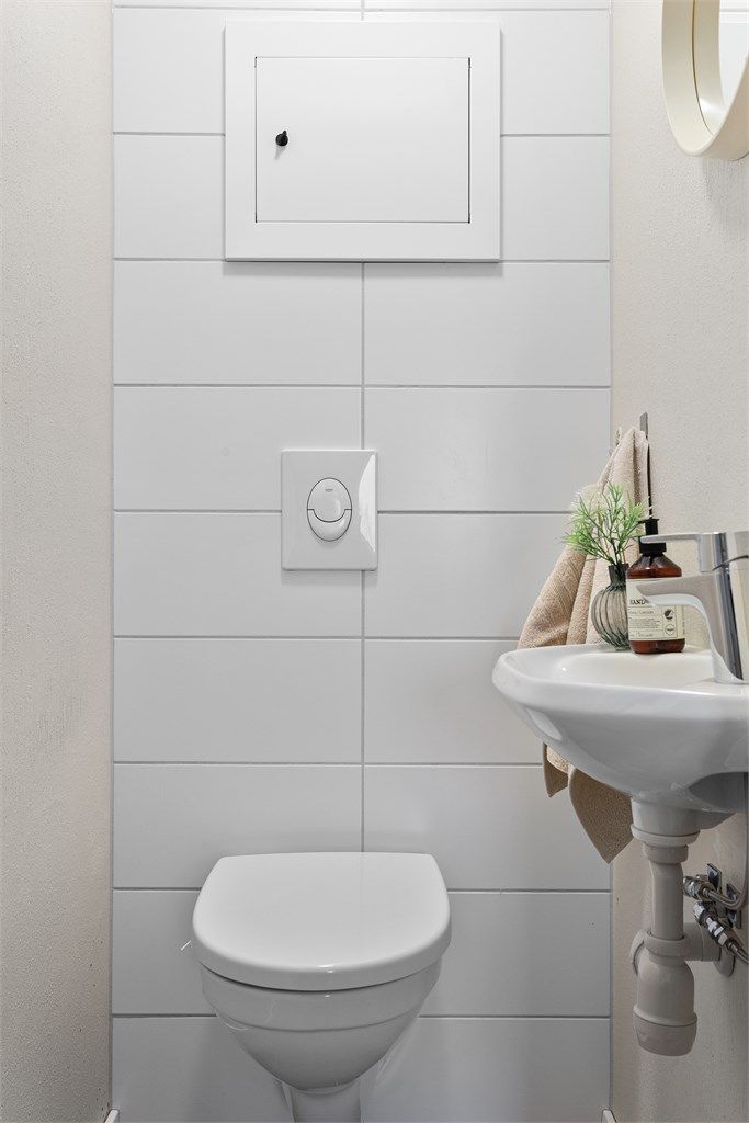 Toalettrom med flislagt gulv innredet med vegghengt toalett og servant.