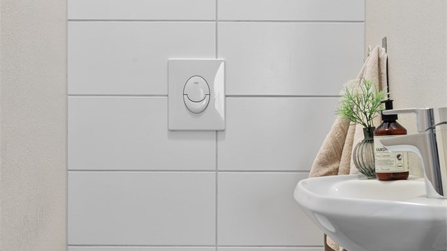 Toalettrom med flislagt gulv innredet med vegghengt toalett og servant.