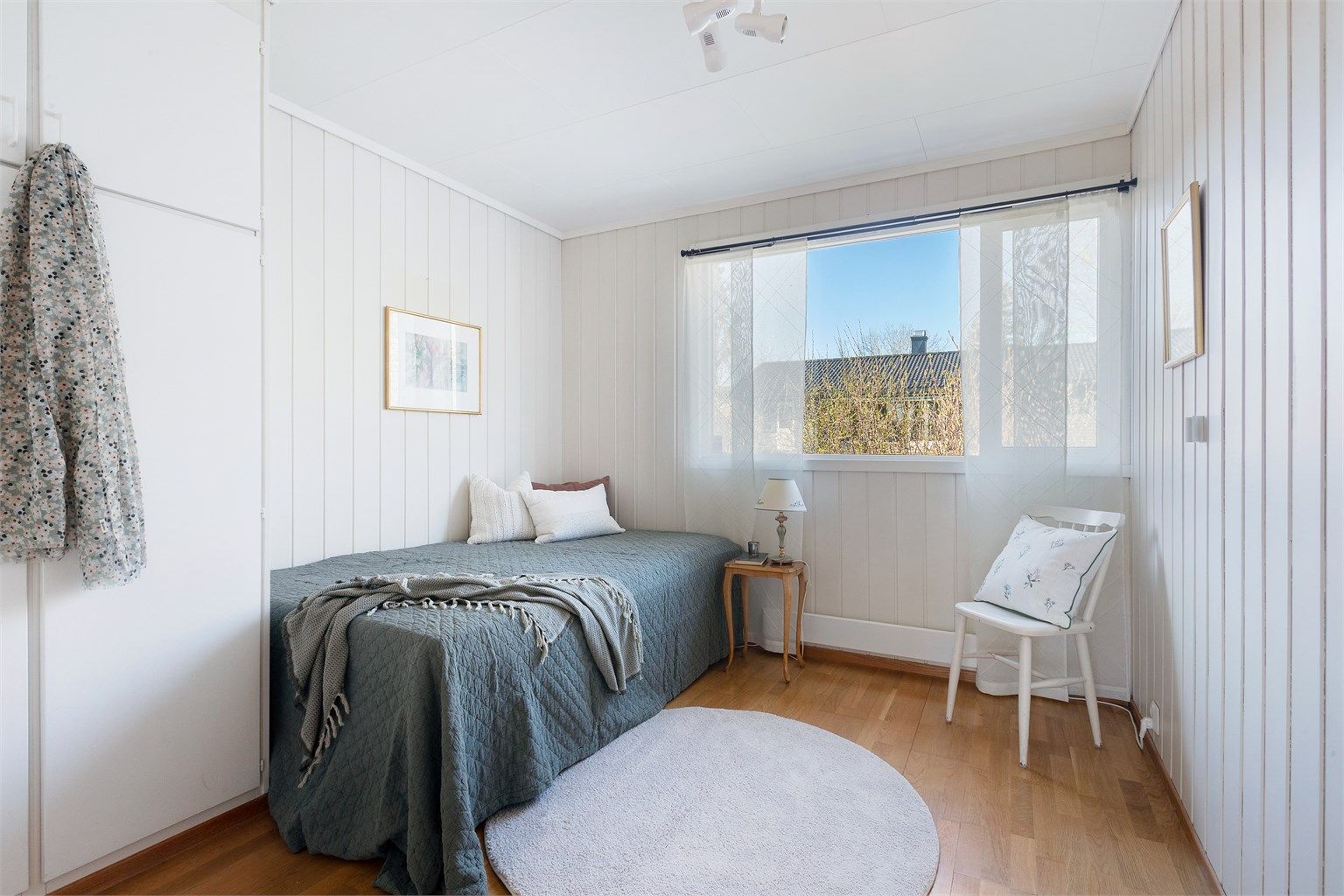 Soverom med panel på veggene og plass til seng og oppbevaring.