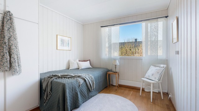 Soverom med panel på veggene og plass til seng og oppbevaring.