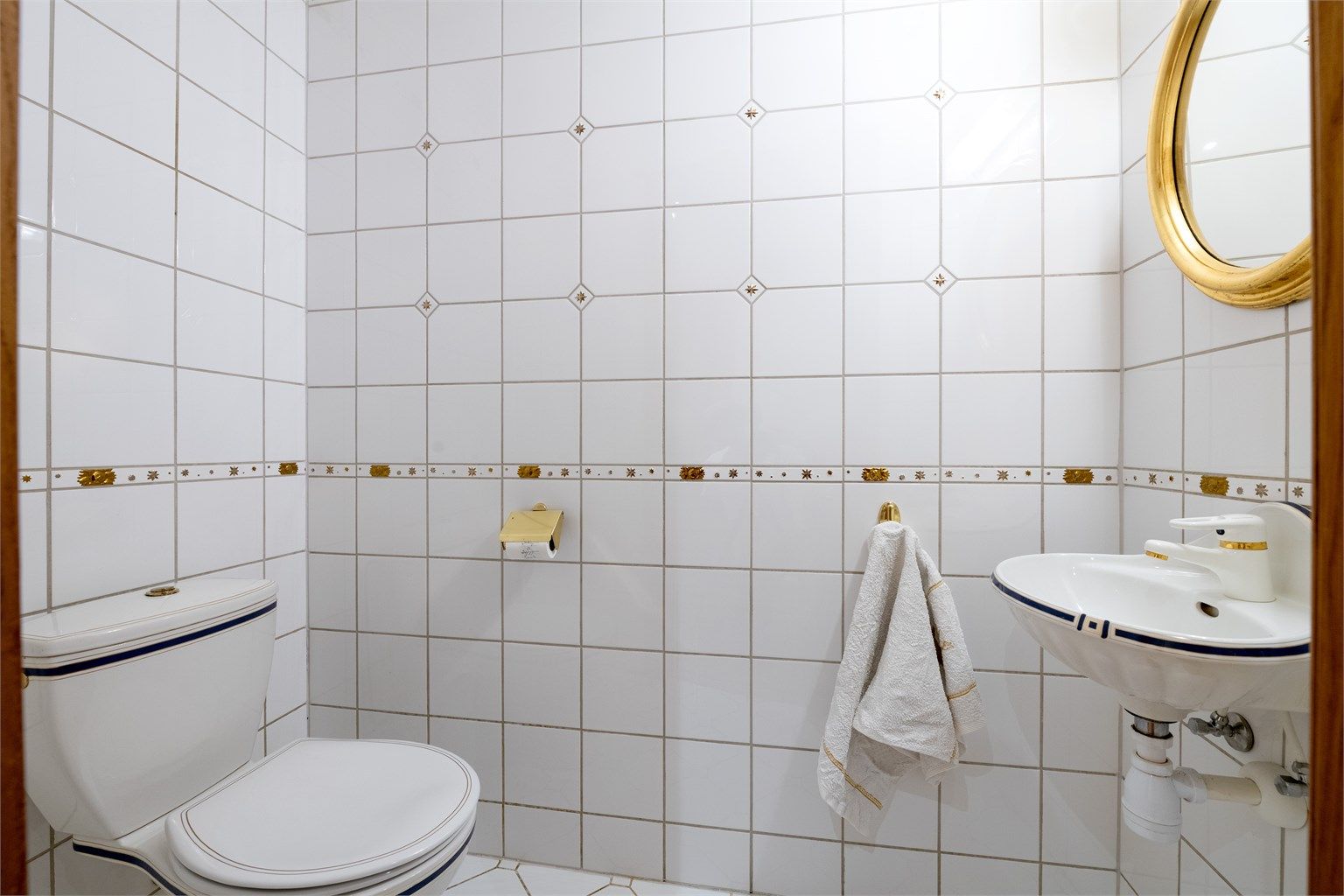 Toalettrom med flislagte overflater, servant og toalett.