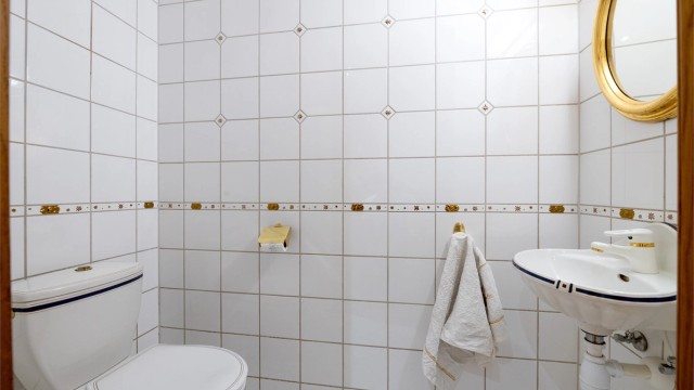 Toalettrom med flislagte overflater, servant og toalett.