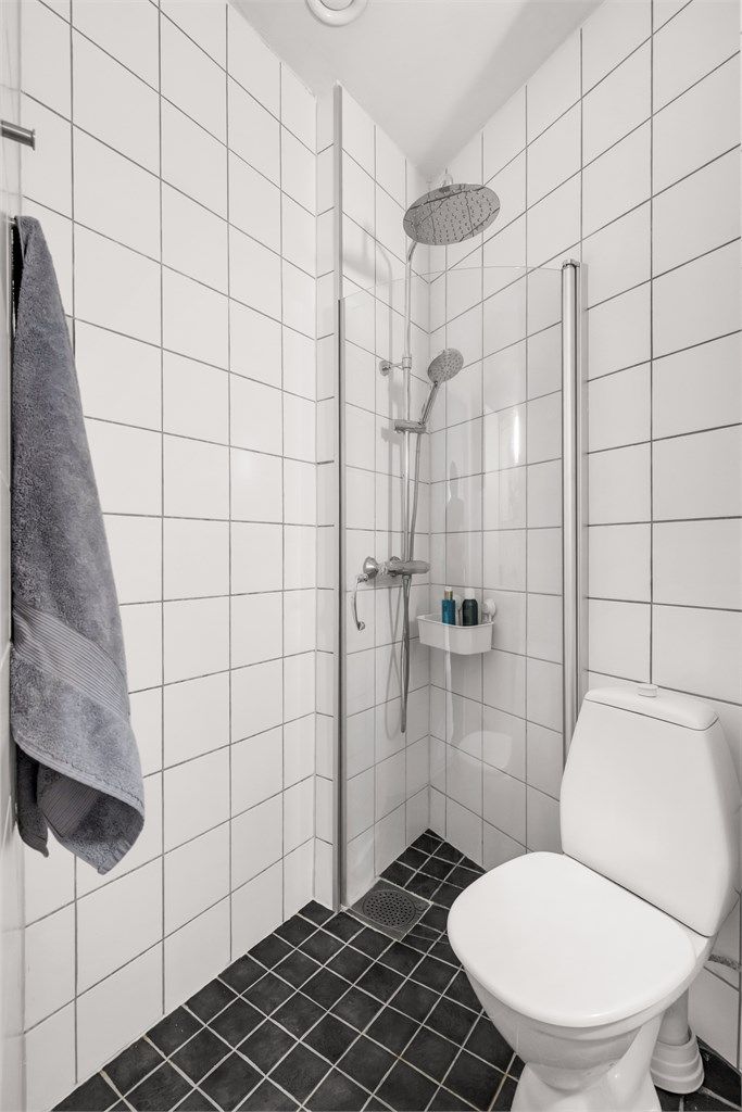 Videre er det gulvstående toalett og egen dusjsone med glassdør med armatur som er tilkoblet både hånd- og regndusj.