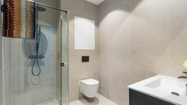 Det ande baderommet er utført i samme stil som det første. Badet er innredet med vegghengt toalett, dusjhjørne og servantmøbel.