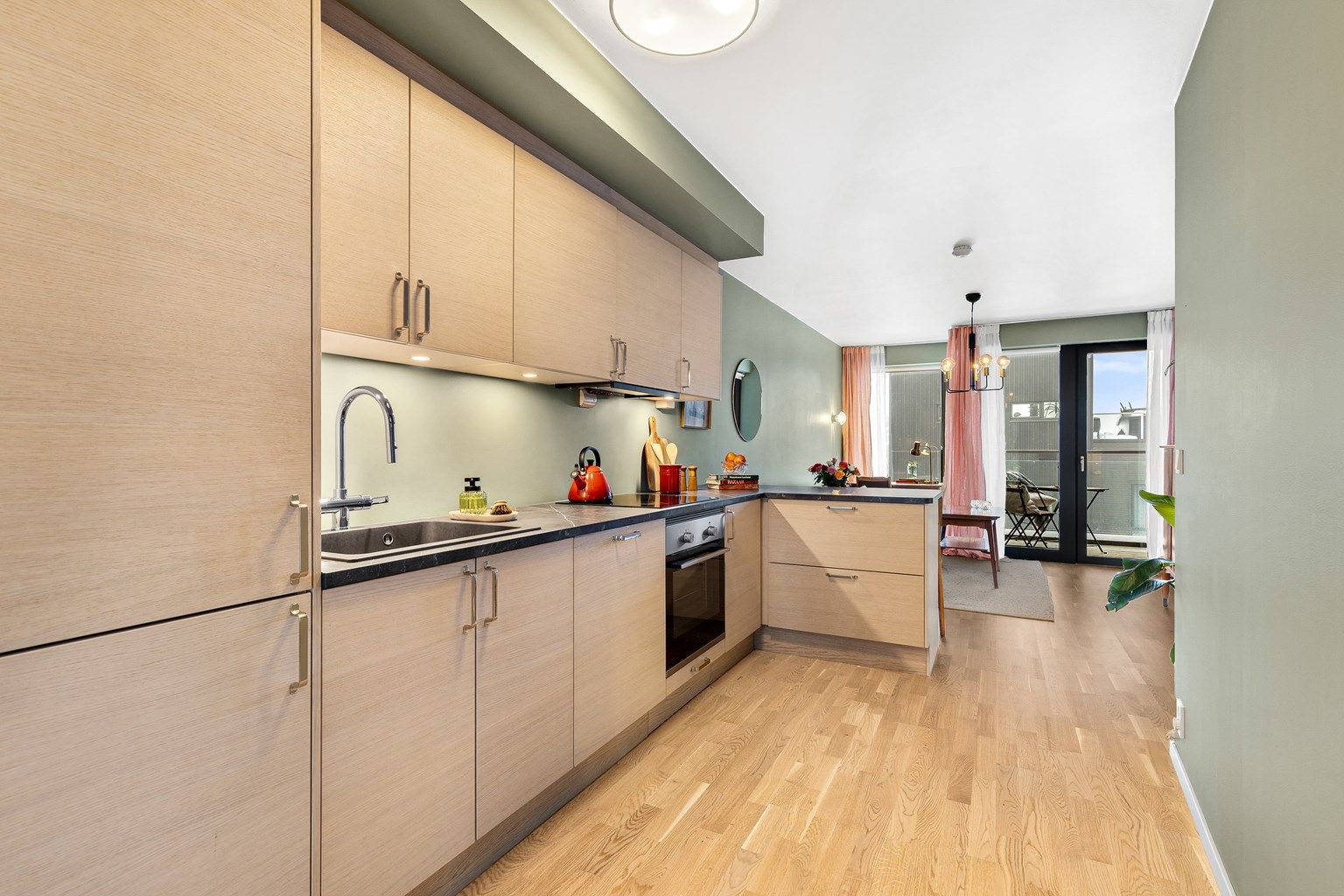 Åpen kjøkkenløsning mot stue. Kjøkkeninnredning med slette fronter. Malt flate mellom overskap og benkeplater av laminat.