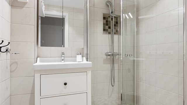 Badet har innredning med servant og dusjhjørne med foldbare glasvegger og vegghengt dusjarmatur med hånddusj og regndusj