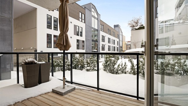 Terrasse med utvendig belysning, strømuttak, terrassebord på gulv og glassrekkverk.