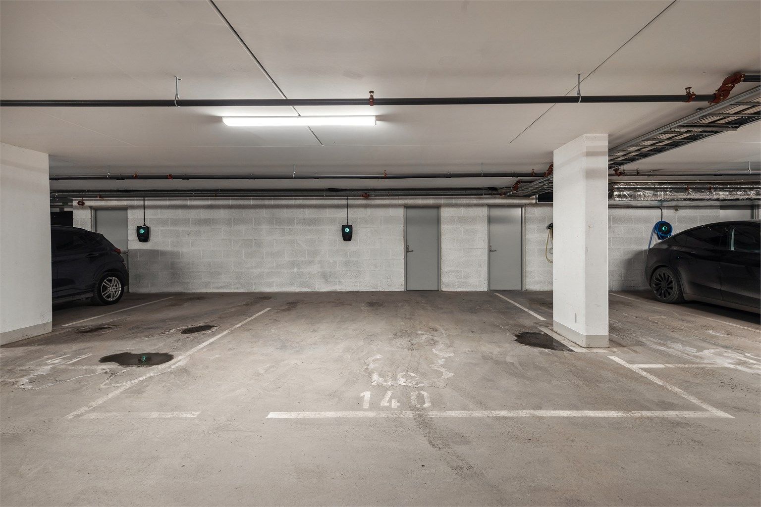 Stor parkeringsplass i lukket garasjeanlegg med lader for elbil montert.