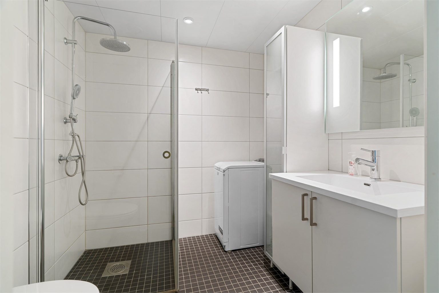 Badet på 5 kvm er pent flislagt med varme i gulvet, downlights i himling og opplegg for vaskemaskin. Badet innredet med servantskap med overskap og speil med lys, vegghengt toalett og dusjhjørne. 