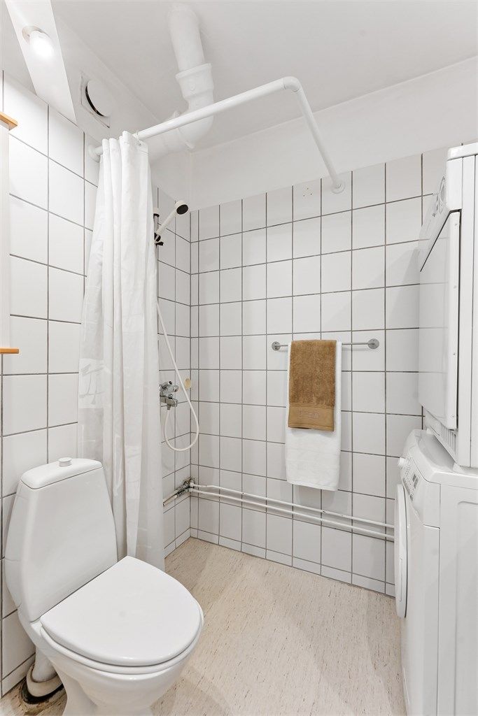 Baderom med gulvbelegg, fliser på vegger, malt himling, vegghengt servantinnredning, vegghengt skap med speil over servant, dusjhjørne, toalett, vaskemaskin og tørketrommel