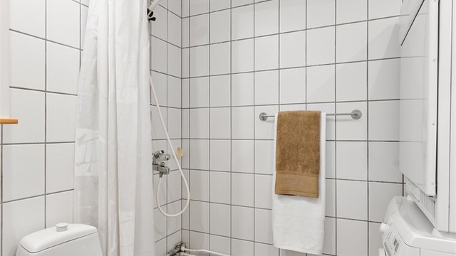 Baderom med gulvbelegg, fliser på vegger, malt himling, vegghengt servantinnredning, vegghengt skap med speil over servant, dusjhjørne, toalett, vaskemaskin og tørketrommel