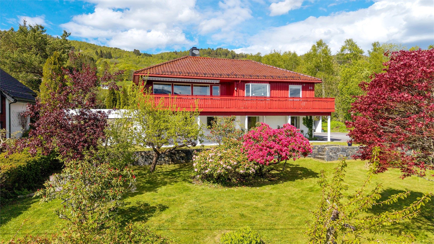 Tomten er pent opparbeidet med plen, beplantning og natursteinsmur.