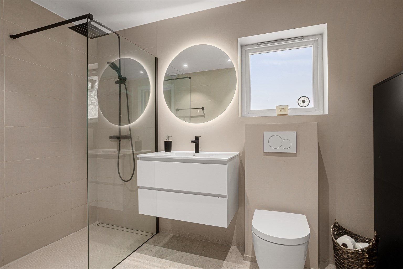 Innredet med dusjhjørne med skillevegg av glass, vegghengt toalett samt vegghengt servantskap med speil og integrert belysning