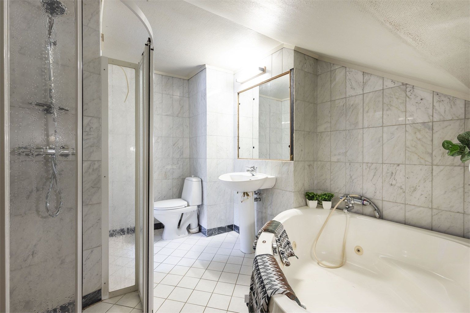 Badet inneholder dusjnisje, badekar, servant og toalett