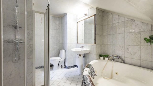 Badet inneholder dusjnisje, badekar, servant og toalett