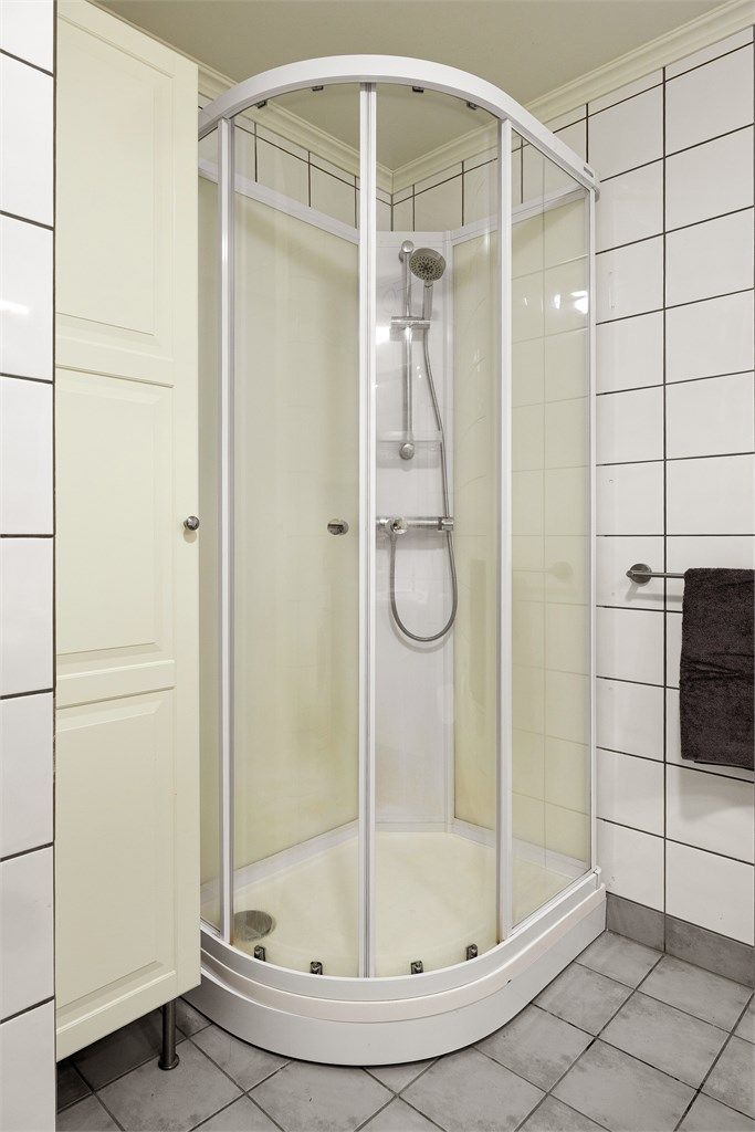 Badet er utstyrt med dusjkabinett og flislagte overflater på gulv og vegger.
