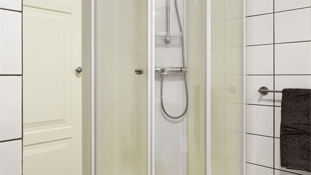 Badet er utstyrt med dusjkabinett og flislagte overflater på gulv og vegger.
