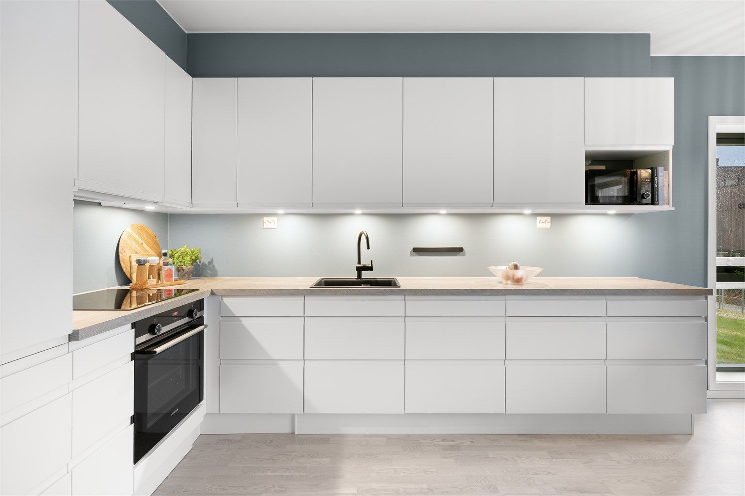 Kjøkkeninnredning fra HTH (2022) med glatte fronter, laminert benkeplate og integrerte hvitevarer.