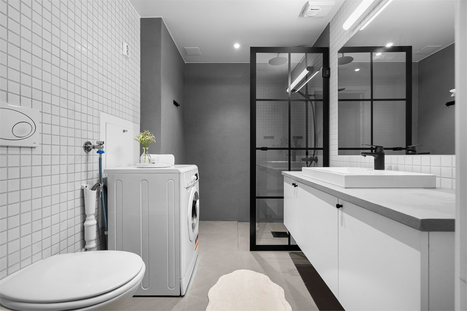 Badet er fra byggeår med oppgraderinger i 2021. Her er det blant annet opplegg for vaskemaskin, gulvflater med gulvvarme belagt med mikrosement (2021), flislagte vegger og mikrosement samt nedsenket himling med downlights.
