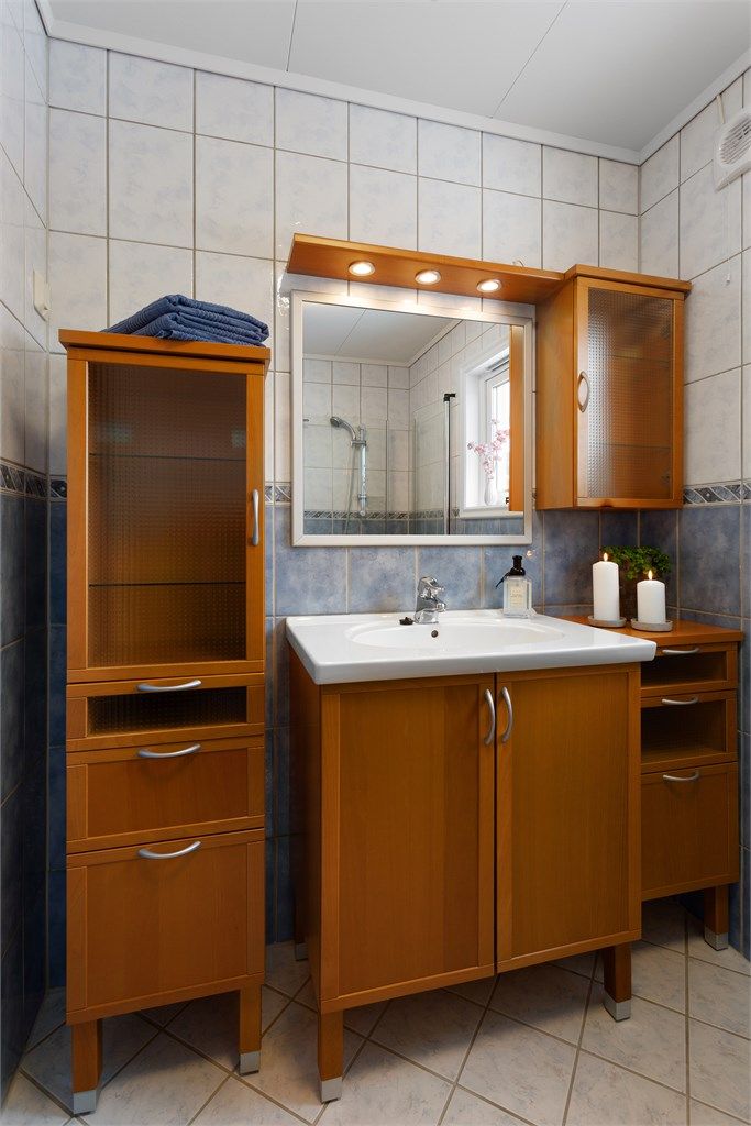 Speil og lys på vegg over servant. Dusjhjørne med glassdører og gulvstående toalett.