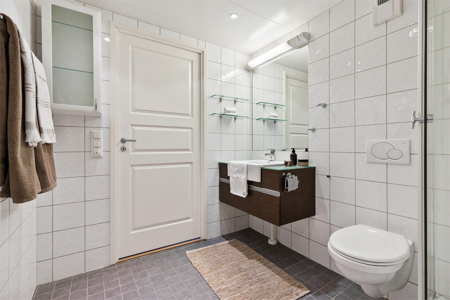 Baderom fra byggeår. Flislagt gulv med gulvvarme. Flislagte vegger. Takplater i himling. Vegghengt servantinnredning. Speil med overlys.