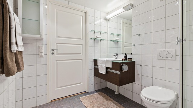 Baderom fra byggeår. Flislagt gulv med gulvvarme. Flislagte vegger. Takplater i himling. Vegghengt servantinnredning. Speil med overlys.