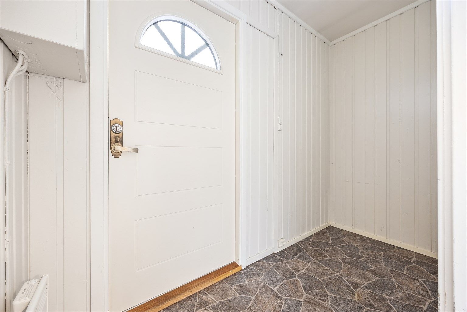 Entré med gulvbelegg og malt panel på veggene.