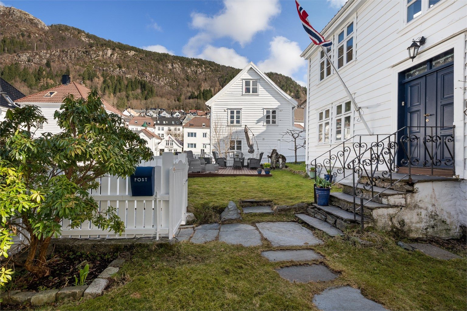 Eiendommen er fint rammet inn av hvitmalt stakittgjerde og med skiferheller frem til inngangen. 
Foto: Her Fotograf 