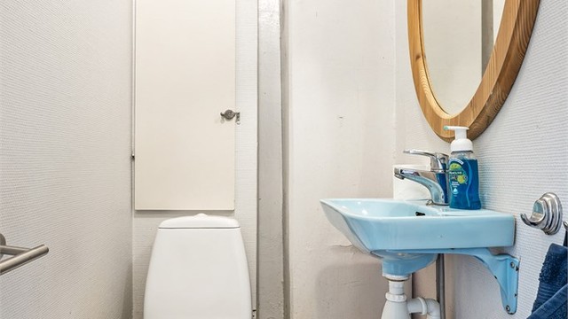 Toalettrom i 1. etasje med gulvstående toalett og vegghengt servant med speil over.