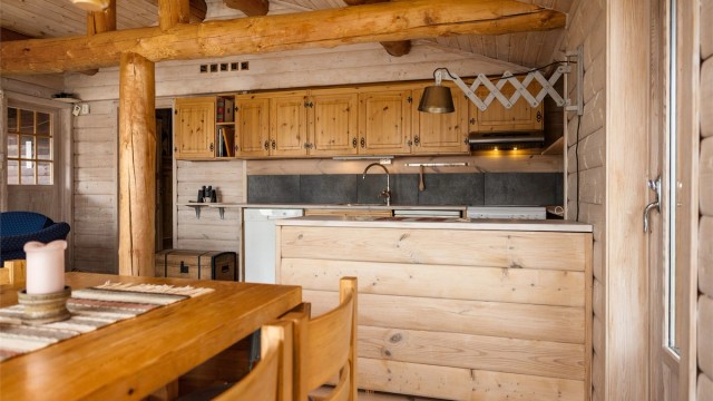 Innredningen fra byggeår med profilerte fronter, kjøkkenøy og benkeplate av tre. Det er frittstående komfyr, oppvaskmaskin og kjøleskap