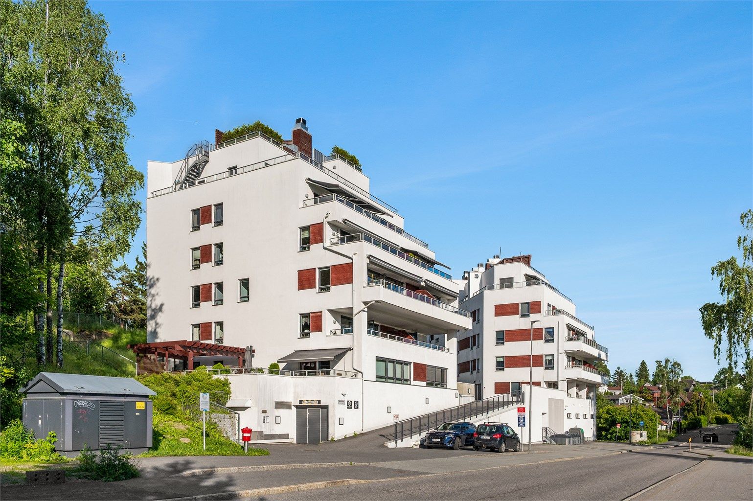 Fasade. Gjesteparkering rett utenfor blokken samt noen inne i garasjeanlegget. 