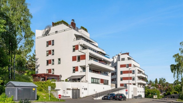 Fasade. Gjesteparkering rett utenfor blokken samt noen inne i garasjeanlegget.