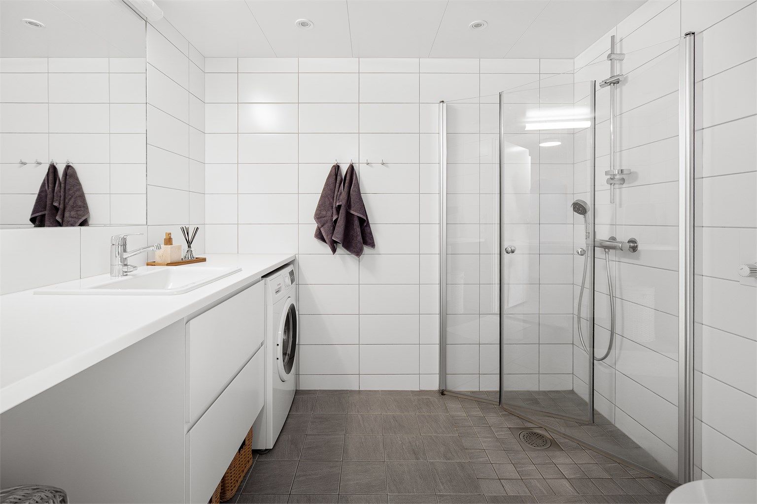 Videre er det dusjhjørne med glassdører og vegghengt dusjarmatur.