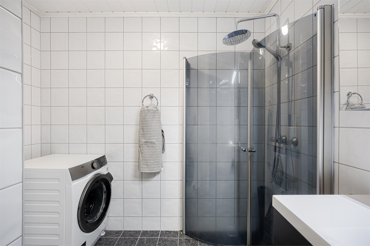 Badet er kombinert vaskerom med opplegg for vaskemaskin. Dusjhjørnet har svingdører og regnfallsdusj.