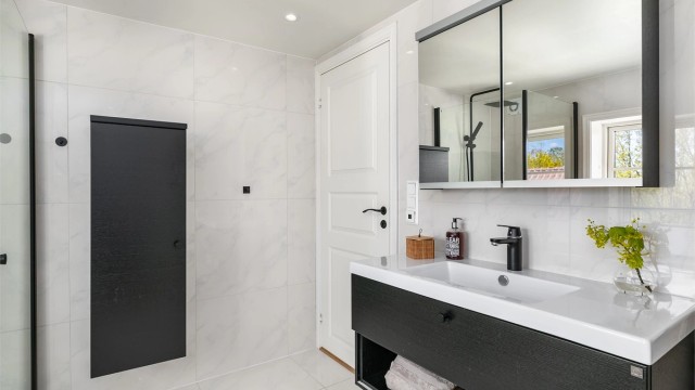 I loftsetasjen inngår også hovedbadet, med marmorerte hvite storformat fliser på gulv og vegger mot møbler og garnityr i kontrasterende sort.