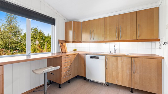 IKEA kjøkkenløsning fra ukjent årstall med innredning i glatte fronter og laminert benkeplate. Flislagt vegg mellom benkeplate og overskap, med belysning under overskap og stikkontakter.