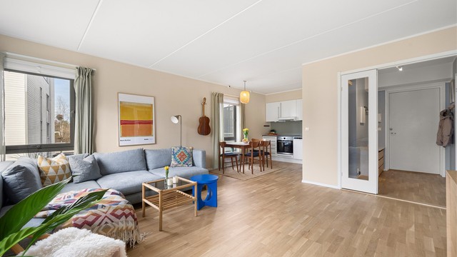 Den delvis åpne løsningen mellom stue og kjøkken skaper en sosial og luftig sone, perfekt for samvær med familie og venner.