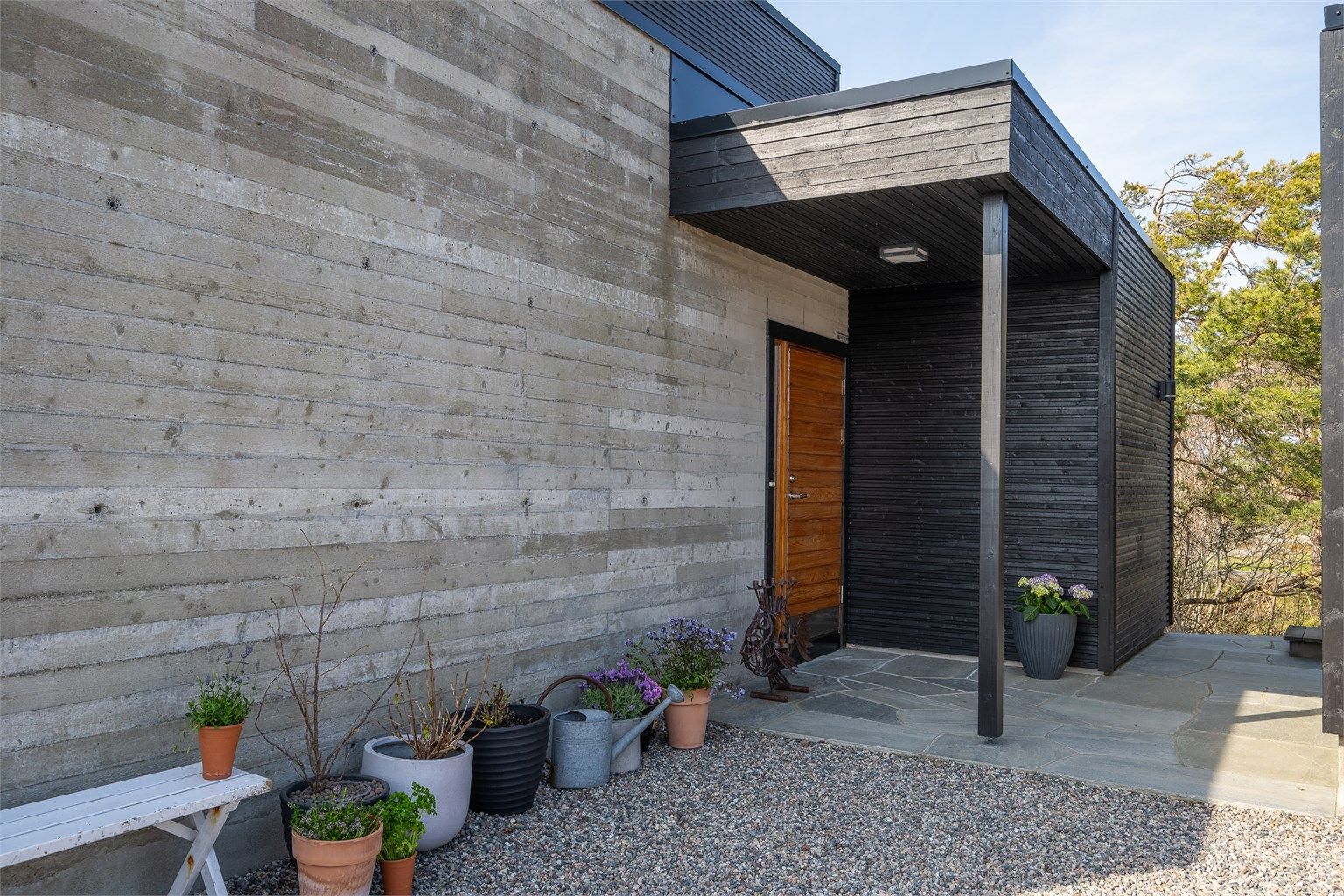 Inngangspartiet er innbydende og kombinerer liggende trekledning med en støpt platting belagt med naturskifer.