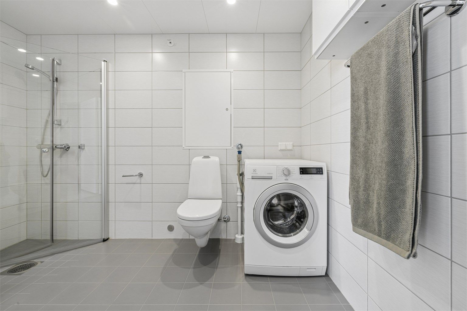 Badet har dusjhjørne med glassdører, vegghengt toalett og opplegg for vaskemaskin.