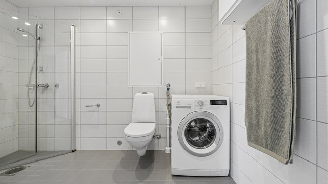 Badet har dusjhjørne med glassdører, vegghengt toalett og opplegg for vaskemaskin.