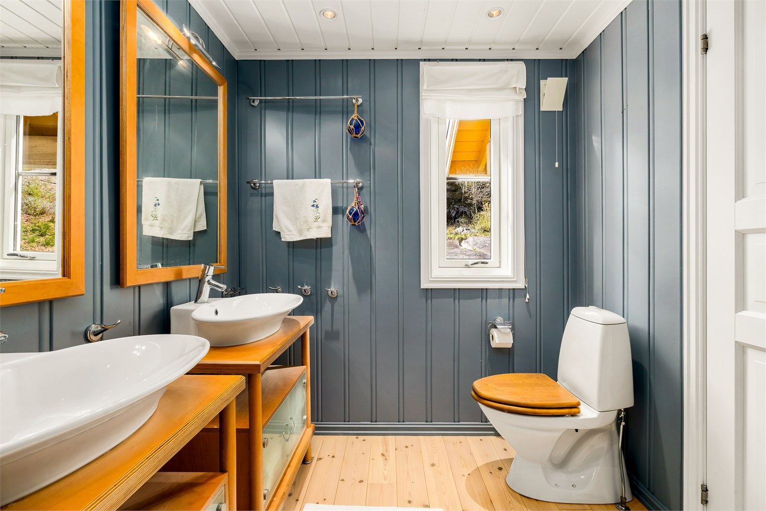 Lyst og romslig bad i 1. etasje med malte overflater og klassisk tregulv. Rommet er smakfullt innredet med to servanter med store speil, høyskap, og møblet er i solid heltre. Dusjkabinett og toalett er montert.