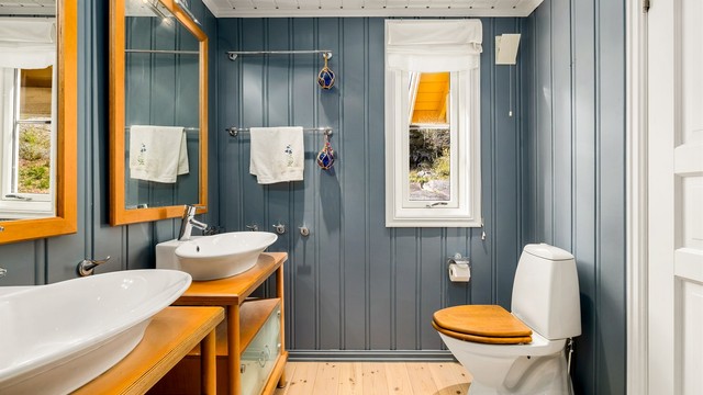 Lyst og romslig bad i 1. etasje med malte overflater og klassisk tregulv. Rommet er smakfullt innredet med to servanter med store speil, høyskap, og møblet er i solid heltre. Dusjkabinett og toalett er montert.