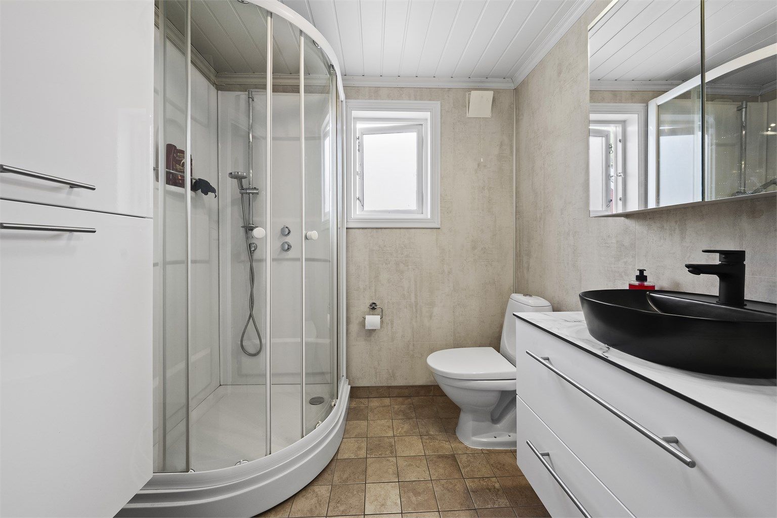 Badet i 1. etasje har flislagt gulv med varmekabler, baderomsplater på vegger og panel i himling. 