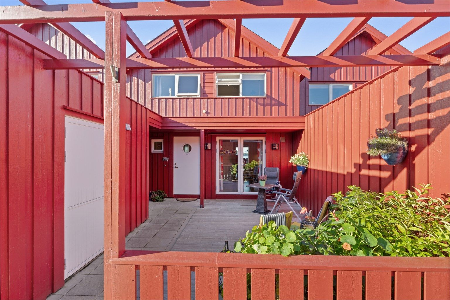 Skjermet terrasse belagt med terrassebord og betongheller ved inngangen.